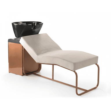 This image features a modern salon shampoo unit designed for professional hair washing services. It consists of a long, upholstered chaise-style reclining bed with a light beige or cream-colored cushion, supported by a continuous tubular metal frame with a copper-toned finish. At one end, there is a compact cabinet-like structure, also with a copper-toned metallic finish, which integrates a glossy black ceramic or plastic shampoo basin. The basin includes an indented area for neck support, suggesting it is a fixed unit for client comfort during hair washing. The overall design is sleek and contemporary. — 3D model (AI enhanced source)