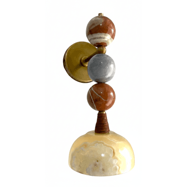 A wall-mounted lamp with a decorative design. The lamp features a circular brass mounting plate.  Extending from the plate is a vertical rod that supports three stacked spherical elements made of natural stone. The top sphere has brown and white banding. The middle sphere is grey. The bottom sphere mirrors the top one with brown and white banding. Below the spheres, a small, conical element wrapped in what appears to be twine or a similar material connects to a dome-shaped base, also made of natural stone with translucent yellow and white marbling. — 3D model (AI enhanced source)