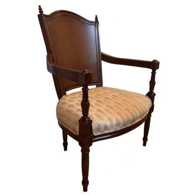 A traditional armchair featuring dark-stained carved wood construction and an upholstered seat. The chair has a solid wood back panel framed by a curved top rail with decorative finials. The front legs and arm supports are turned and fluted, showcasing intricate detailing. The seat cushion is upholstered in a multi-colored geometric patterned fabric, predominantly beige with accents of pink and green. — 3D model (AI enhanced source)