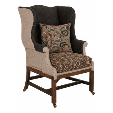 A wingback chair featuring a high back with distinctive 'wings', upholstered in a combination of two fabric types. The primary upholstery is a textured neutral fabric on the sides and lower back, with a darker, possibly charcoal-colored fabric on the upper back and arms. Decorative brass nailhead trim outlines the transition between fabrics and along the seat base. It includes a seat cushion and a decorative throw pillow. The chair is supported by a wooden frame with four legs, the front two of which are fitted with brass casters. The legs and structural supports are made of dark stained wood. — 3D model (AI enhanced source)