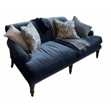 A two-seat sofa featuring a plush dark blue velvet upholstery, rolled armrests, and a skirted base with visible turned wooden legs. It is adorned with several throw pillows and a knitted blanket, suggesting a cozy and inviting aesthetic. — 3D model (AI enhanced source)