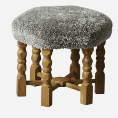 A small, round stool featuring a soft, shaggy grey upholstered seat and four turned wooden legs with stretcher supports. The legs have a light brown wood finish, and the overall design combines rustic and cozy elements. — 3D model (AI enhanced source)