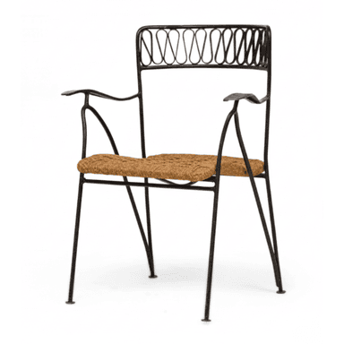 An armchair featuring a black wrought iron frame with slender legs and curved armrests. The backrest is adorned with an intricate, repeating scrolled pattern. The seat is constructed from tightly woven natural rush material, providing a textural contrast to the metal frame. The design evokes a classic bistro or Mediterranean aesthetic. — 3D model (AI enhanced source)
