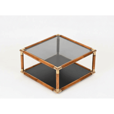 A square, two-tiered coffee table featuring a frame constructed from bamboo-style wood and joined by polished brass corner connectors. The top surface is a rectangular panel of smoked glass, while the lower shelf is a solid, opaque black surface, providing additional storage or display space. The design exudes a mid-century modern or Hollywood Regency aesthetic. — 3D model (AI enhanced source)