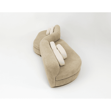 A contemporary curved modular sectional sofa upholstered in a beige, textured fabric. The sofa features a serpentine or S-shaped configuration, comprising multiple rounded segments. It is designed with a low profile and includes several rectangular, lighter-colored lumbar pillows for added comfort. The overall aesthetic is soft and organic, suitable for modern interior spaces. — 3D model (AI enhanced source)