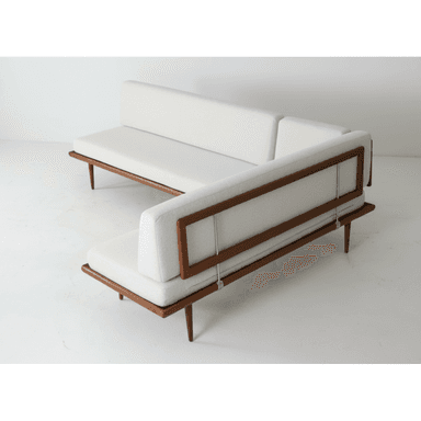 An L-shaped sectional sofa featuring an exposed dark-stained wooden frame, likely teak, supporting thick, light-colored upholstered cushions. The sofa consists of two distinct segments forming a right-angle configuration. The backrests are also upholstered and appear to be slightly reclined, secured within the wooden frame with visible metal supports. The frame rests on slender, tapered wooden legs. — 3D model (AI enhanced source)