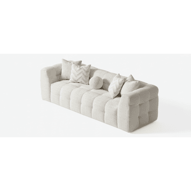A long, low-profile contemporary sofa upholstered in a light beige, textured fabric. It features deep, square tufting across the seat, backrest, and integrated armrests, creating a plush and inviting appearance. Several decorative pillows in matching and complementary patterns are arranged on the sofa. — 3D model (AI enhanced source)
