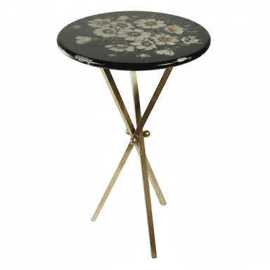 A small, round black table featuring a multi-color floral motif painted on its lacquered top, supported by a gold-toned metal X-frame base. The tabletop shows visible wear and chipping along its edges, revealing lighter material beneath the black finish. The base consists of four slender, straight legs, joined at the center in an X-shape. — 3D model (AI enhanced source)