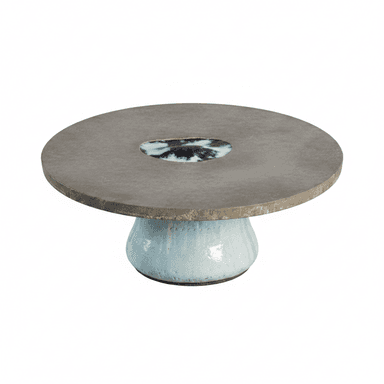 A low, circular accent table featuring a concrete top and a ceramic base. The rough-textured concrete top incorporates a central, irregularly shaped inlay of glazed ceramic in shades of blue and white. The base is a bulbous, hand-glazed ceramic form with a light blue/aqua finish, showing organic variations and a subtly textured surface. The overall design suggests an artisanal, wabi-sabi aesthetic. — 3D model (AI enhanced source)