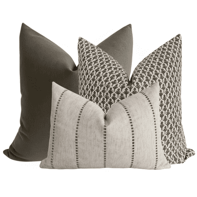 A set of three decorative throw pillows. One pillow is a solid dark grey, likely velvet or a similar soft fabric. Another pillow features a repeating pattern of dark brown stylized leaf motifs on a cream background. The third pillow is rectangular and oriented horizontally, with a textured cream fabric and vertical stripes composed of dashed lines in a dark grey or brown hue. The pillows are arranged in a layered composition. — 3D model (AI enhanced source)