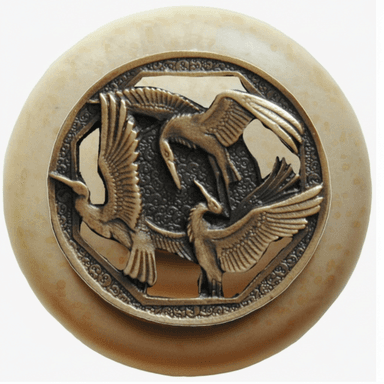 A circular decorative object featuring a central ornate metal medallion embedded into a larger, smooth disc. The medallion is crafted from a bronze-toned metal and depicts three birds (likely cranes or herons) in relief, with spread wings, set within an octagonal frame. The background of the metalwork has a textured, stippled finish. The surrounding circular disc is a light beige or cream color, with a smooth, possibly polished, surface and subtle textural variations. — 3D model (AI enhanced source)