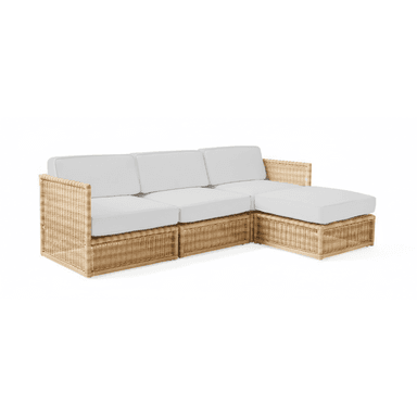 A modern L-shaped sectional sofa featuring a natural woven frame, likely rattan or wicker, with plump white upholstered cushions for the seat and backrests. The design is modular, forming a corner configuration with a chaise extension on one side. The woven material gives it a textured, earthy aesthetic. — 3D model (AI enhanced source)