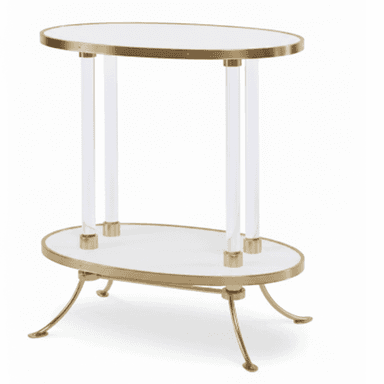 A two-tiered oval accent table featuring a brass-finished metal frame and clear acrylic support columns. Both tiers have white oval surfaces, possibly a faux marble or laminate, encased in brass rims. The table stands on four splayed brass legs with curved feet, extending from the lower tier. — 3D model (AI enhanced source)