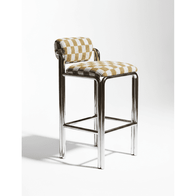 A modern bar stool featuring a sleek, tubular chrome frame and a distinctive checkered upholstered seat and backrest. The frame forms a continuous loop for the legs and incorporates a footrest. The upholstery is a textured fabric in alternating cream and light yellow/beige squares, covering a padded seat and a cylindrical backrest. — 3D model (AI enhanced source)