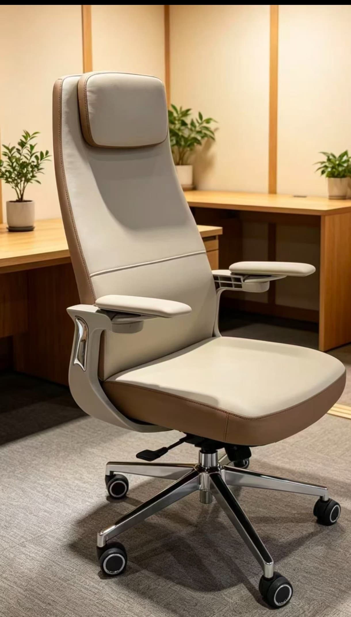 A modern executive office chair upholstered in a two-tone scheme of cream and brown. It features a high back with an integrated headrest, padded adjustable armrests, and a polished metal five-star base equipped with casters for mobility. The chair exhibits an ergonomic design suitable for prolonged use. — 3D model