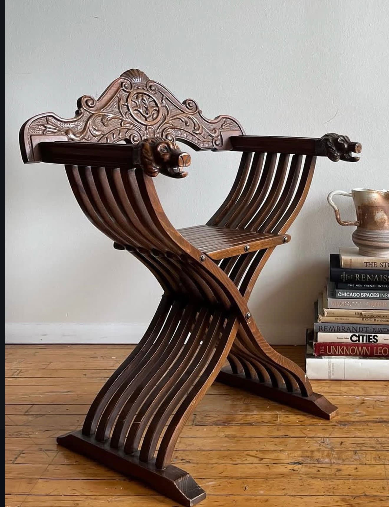 A dark brown carved wood Savonarola chair, also known as a Dante chair, featuring an iconic X-shaped, collapsible frame. The chair has a slatted seat and back, allowing for a comfortable recline. Its armrests are elaborately carved, terminating in decorative lion heads. The backrest is highly ornate, displaying intricate scrollwork and floral motifs, characteristic of Renaissance design. The construction suggests a historical and distinguished piece of furniture. — 3D model