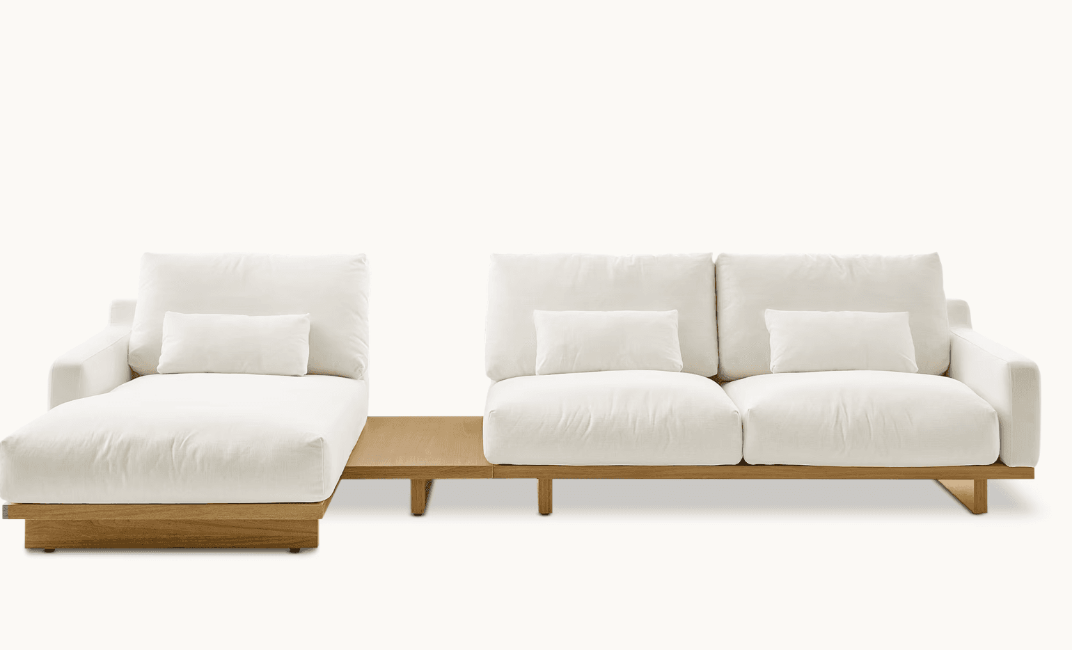 A modular sofa configuration featuring a chaise lounge section and a two-seater section, unified by a natural wood platform base. The seating and back cushions are upholstered in white fabric, and the design includes small rectangular accent pillows. The overall aesthetic is minimalist and modern, with clean lines and a focus on comfort. The wooden base provides a warm, natural contrast to the light upholstery. — 3D model