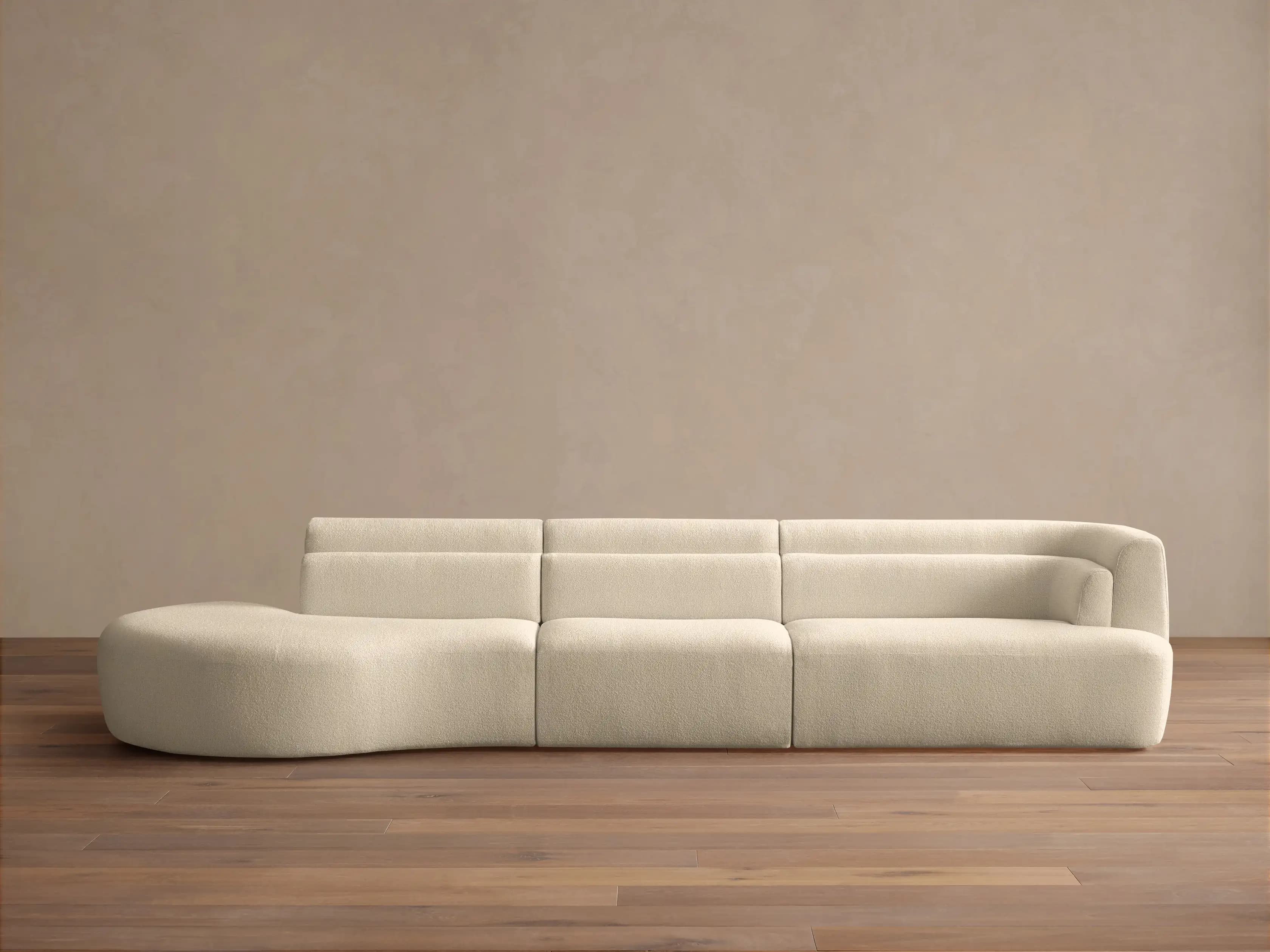 A modular sofa with a rounded chaise lounge on the left side. The sofa features a soft, textured fabric upholstery and a low profile. The back cushions appear to be integrated into the sofa's structure, creating a continuous, streamlined look. The design is modern and minimalist. — 3D model