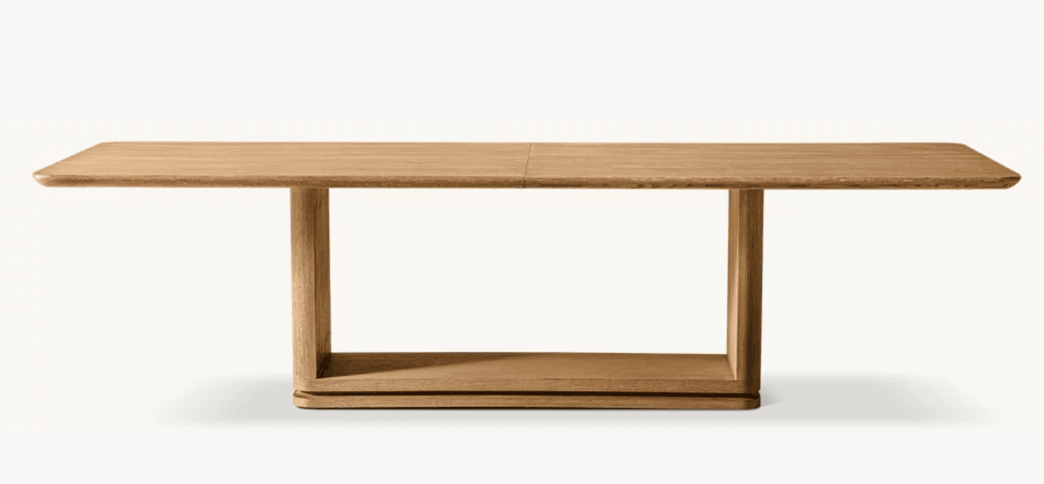 A long, rectangular wooden table featuring a light-toned wood finish and a contemporary design. The tabletop has subtly rounded corners and appears to be made from solid wood or high-quality veneer, with a visible seam suggesting it might be an extendable or modular design. The base consists of two distinct U-shaped leg structures, each with a lower horizontal support that connects the vertical elements, sitting on a slightly recessed plinth-like base. The overall aesthetic is minimalist and robust. — 3D model