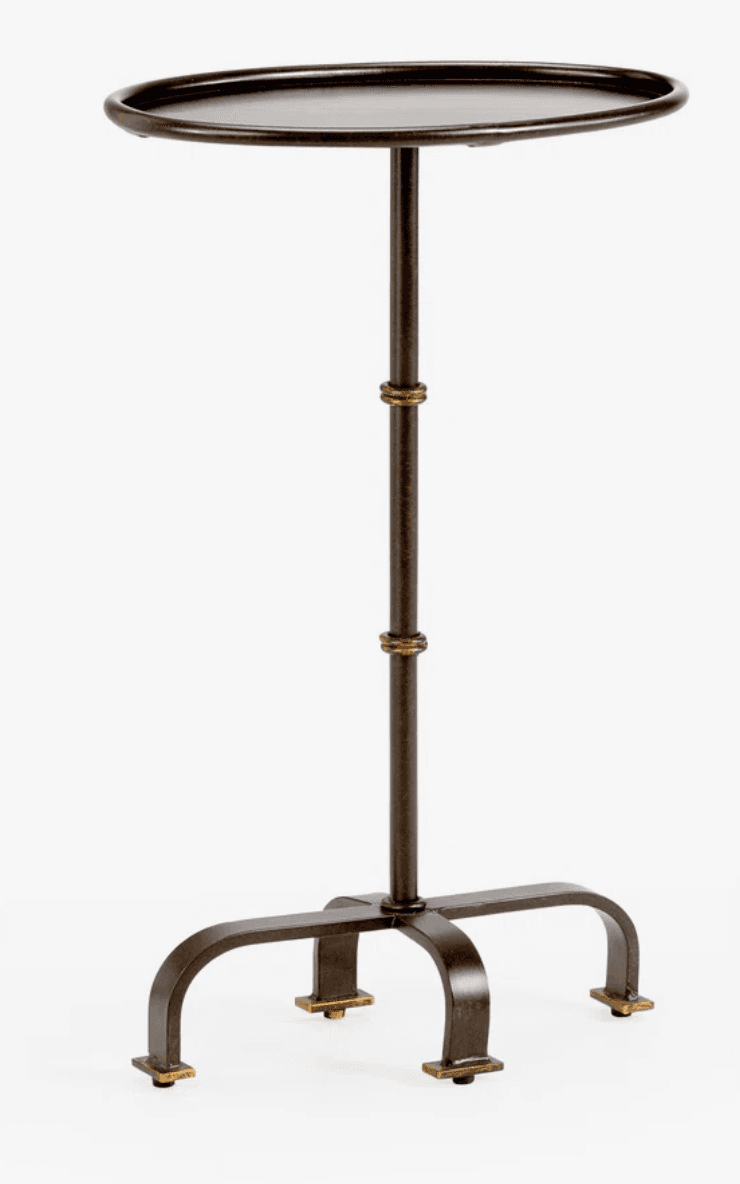 A dark bronze metal accent table featuring a round, shallow tray top, a slender central pedestal, and a three-legged arched base with brass-colored foot pads and decorative rings. — 3D model