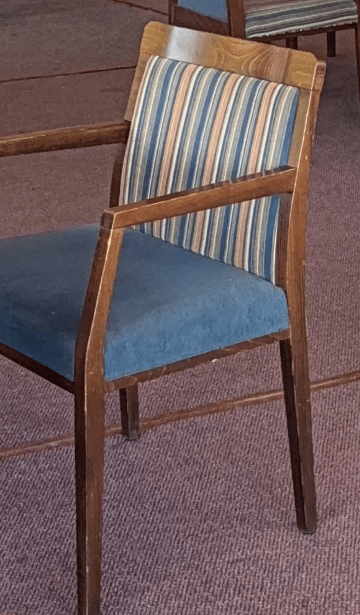 A contemporary armchair featuring a dark wood frame and upholstered seat and back. The seat cushion is upholstered in a solid blue fabric, while the backrest features a vertical stripe pattern in shades of blue, beige, and white. The chair has straight legs and arms, suggesting a sturdy and functional design suitable for various settings. — 3D model