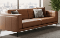 A modern three-seater sofa upholstered in tan leather, featuring distinct track arms and a backrest with subtle square tufting. The seat cushions are smooth, and the sofa rests on slender, tapered black metal legs. Several decorative throw pillows with varying patterns and textures are placed on the sofa. — 3D model