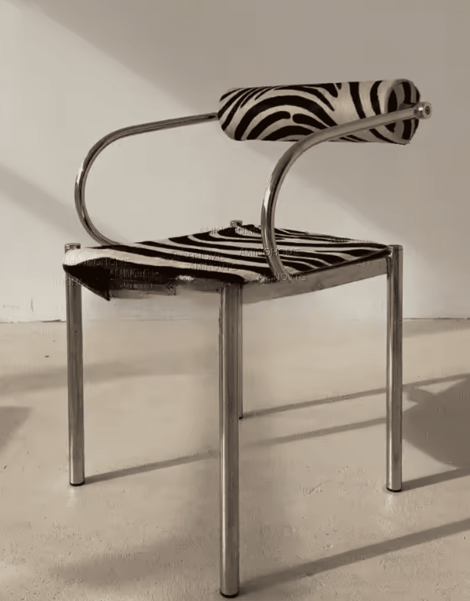 A modern armchair with a chrome-plated tubular metal frame. The seat and backrest are upholstered in fabric with a black and white zebra print pattern. The armrests are formed by curved tubular metal that extends upwards and backwards, supporting a cylindrical, upholstered headrest. — 3D model