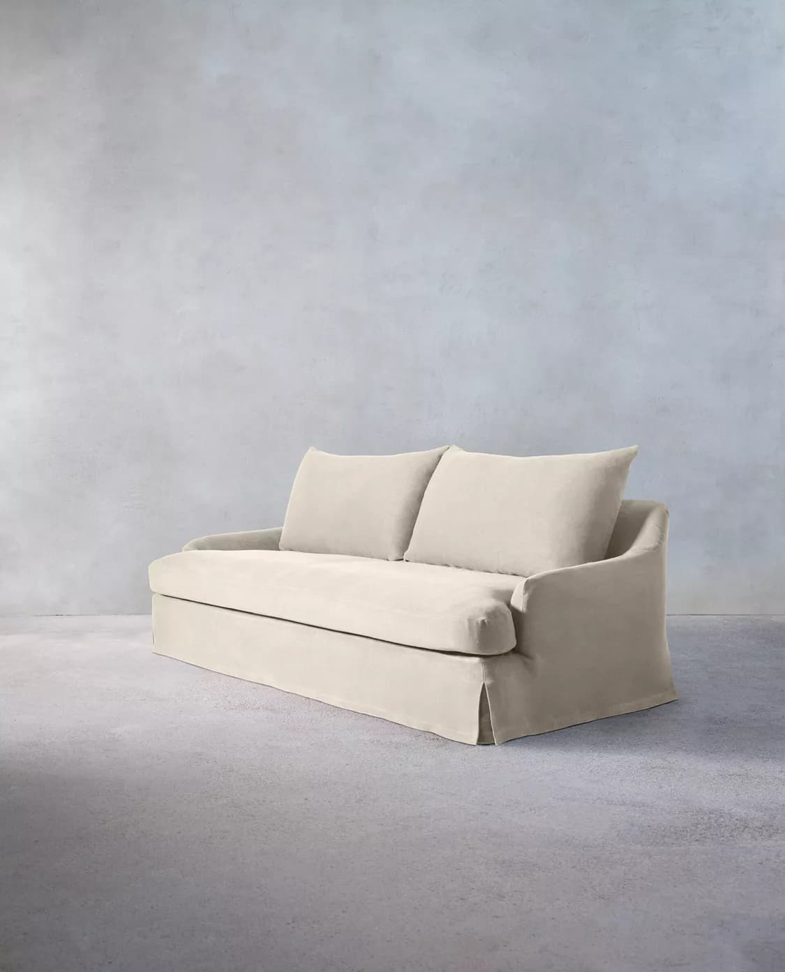A light-colored, slipcovered two-seater loveseat with a casual aesthetic, featuring a skirted base and two separate seat and back cushions. The arms are gently sloped, and the overall appearance is soft and inviting. — 3D model