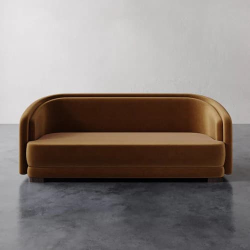 A contemporary loveseat featuring a continuous, rounded backrest and integrated arms upholstered in a plush, camel-colored velvet fabric. The design is characterized by its smooth, curvilinear lines and minimalist profile, resting on a recessed dark wood base. The seat cushion is integrated, contributing to the streamlined appearance. — 3D model