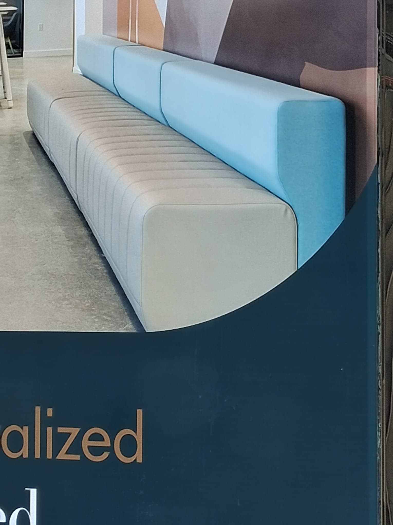 A contemporary modular linear seating unit consisting of three identical seat segments and a continuous backrest made of three corresponding segments. The seat segments are upholstered in a light beige/grey fabric with vertical channel tufting, while the backrest segments are upholstered in a light blue, smooth fabric. The overall design is minimalist and features a low profile. — 3D model