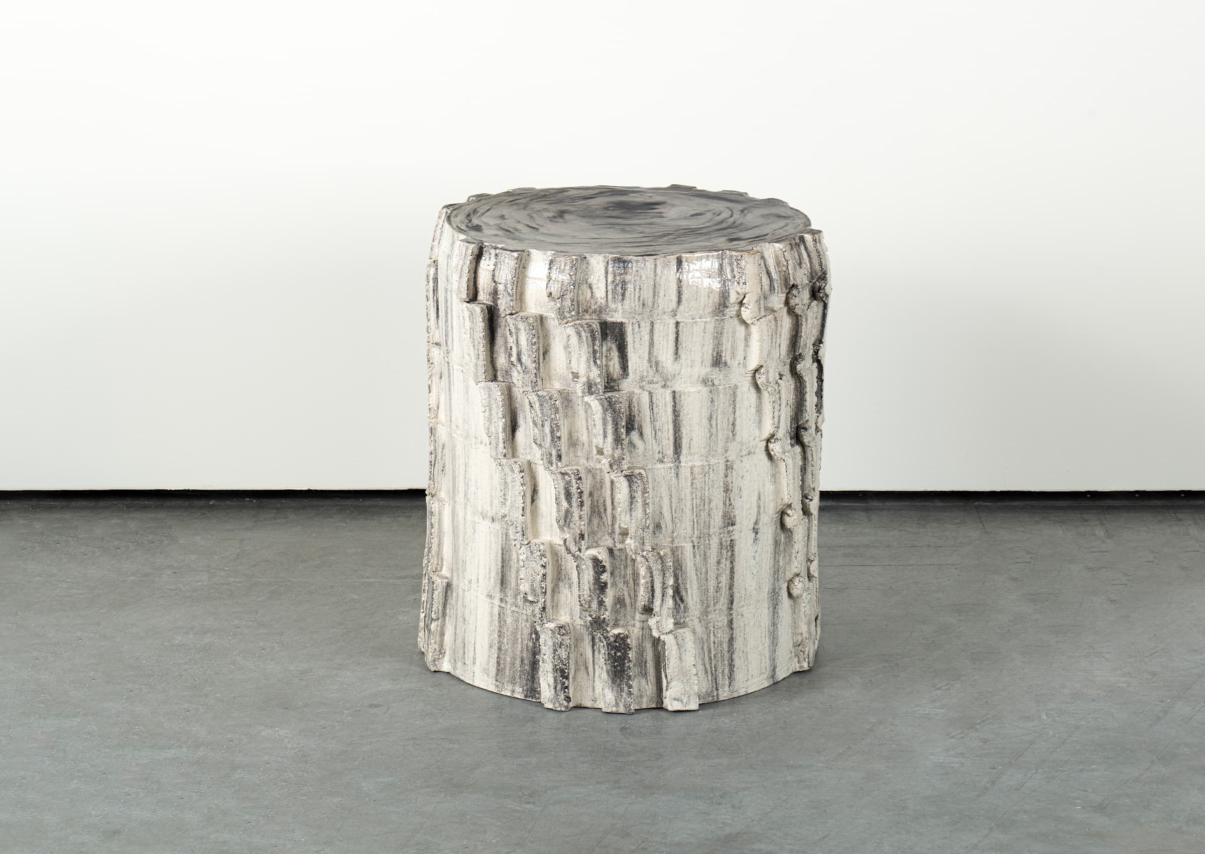 A cylindrical side table with a textured surface resembling tree bark. The top surface has a marbled, glossy finish, while the body features irregular, stacked horizontal segments with a rough, matte texture. The color palette is predominantly off-white and grey, with darker grey or black accents. — 3D model