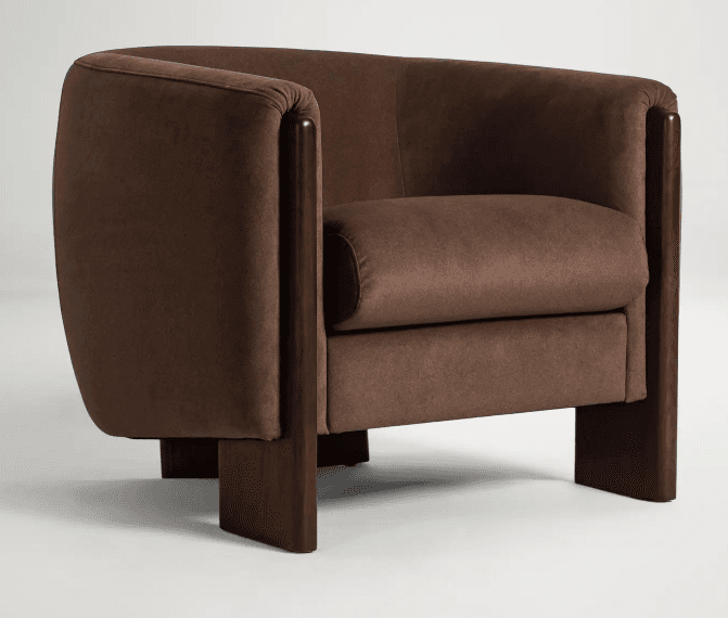 A contemporary armchair featuring a rounded, barrel-shaped back and integrated arms, upholstered in a rich brown fabric. The chair is distinguished by its exposed, dark-stained wood frame that forms both the armrests and the slab-style legs, creating a cohesive and structured appearance. The seat cushion is thick and upholstered in the same material, ensuring comfort. — 3D model
