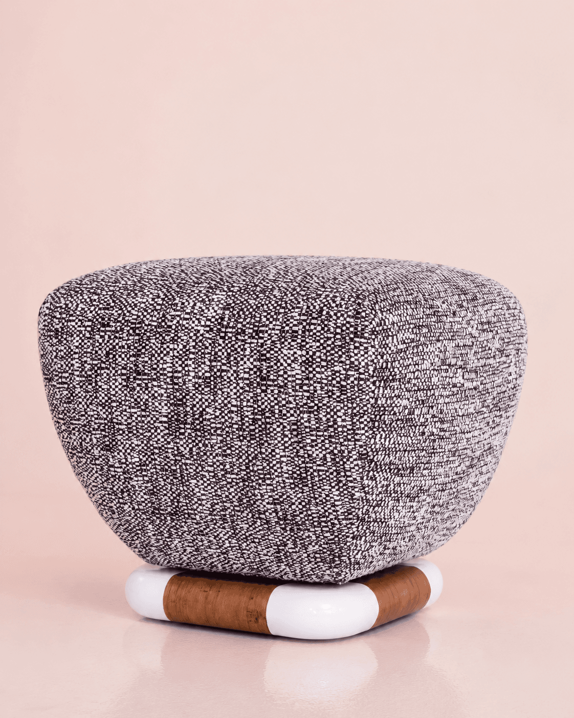 A modern, upholstered footstool featuring a rounded, speckled black and white fabric top and a distinctive circular base made of natural cork with segmented white enamel accents. — 3D model