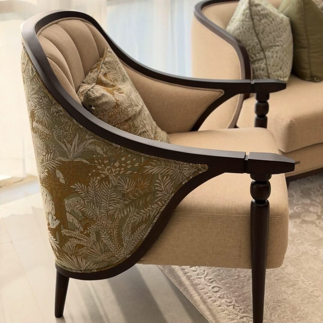 An upholstered armchair featuring an exposed dark wood frame, a beige fabric seat and inner back, and a patterned fabric on the outer back. The inner back is channel tufted, and the front legs are turned. — 3D model
