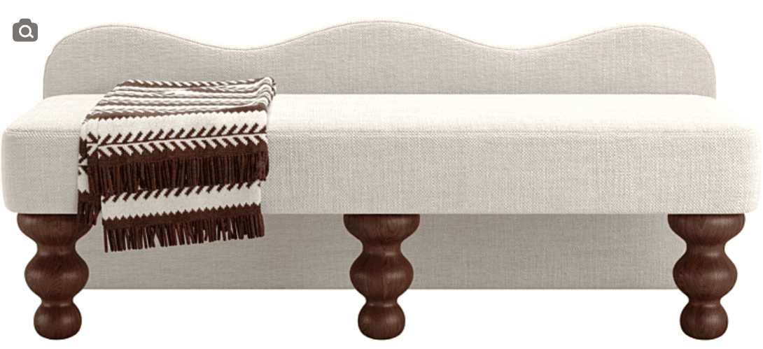 A contemporary upholstered bench featuring a distinct scalloped or wavy backrest. The bench is covered in a light, textured fabric, likely an off-white or cream linen blend. It stands on four dark, turned wooden legs, providing a classic contrast to the modern lines of the upholstered body. A brown and white striped throw blanket is draped over one end of the bench, adding a touch of warmth and texture. — 3D model