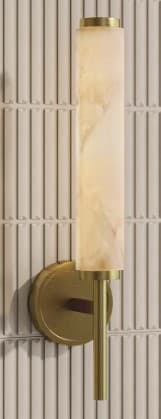 A modern wall sconce featuring a cylindrical alabaster shade mounted on a brushed brass fixture. The light diffuses through the translucent alabaster, revealing natural veining, and is supported by a slender brass arm extending from a circular wall plate. — 3D model