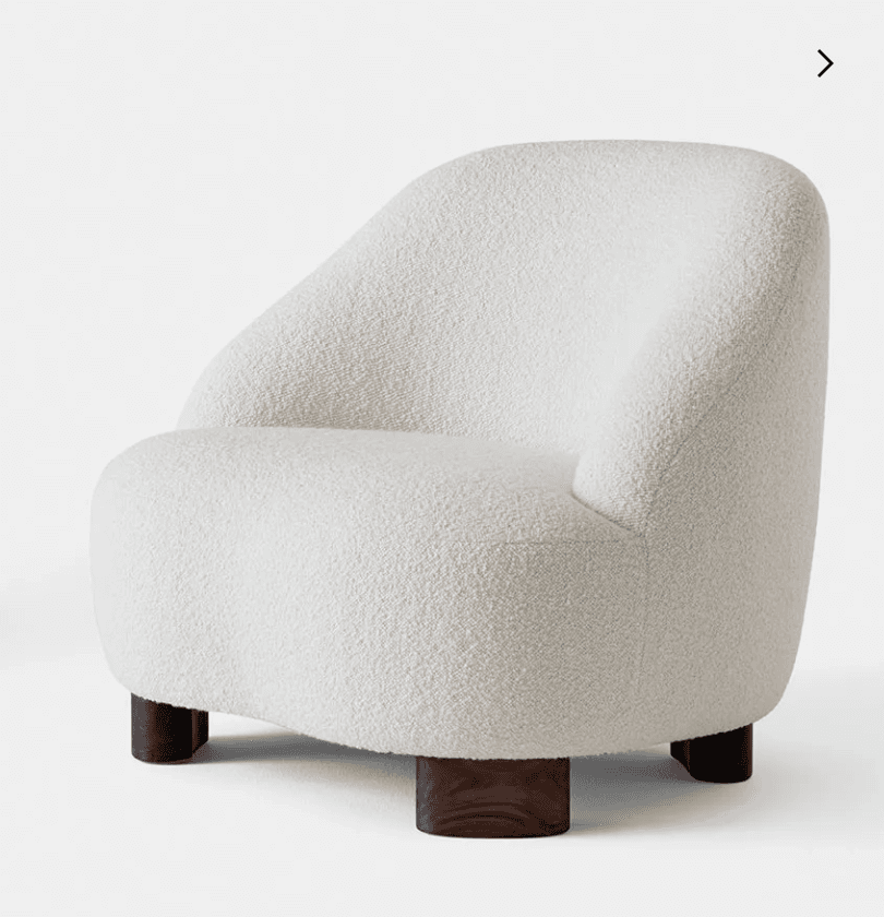 A contemporary lounge chair featuring a rounded, sculptural silhouette and upholstered in a cream-colored bouclé fabric. The chair sits low to the ground on four dark, cylindrical wooden block legs. — 3D model