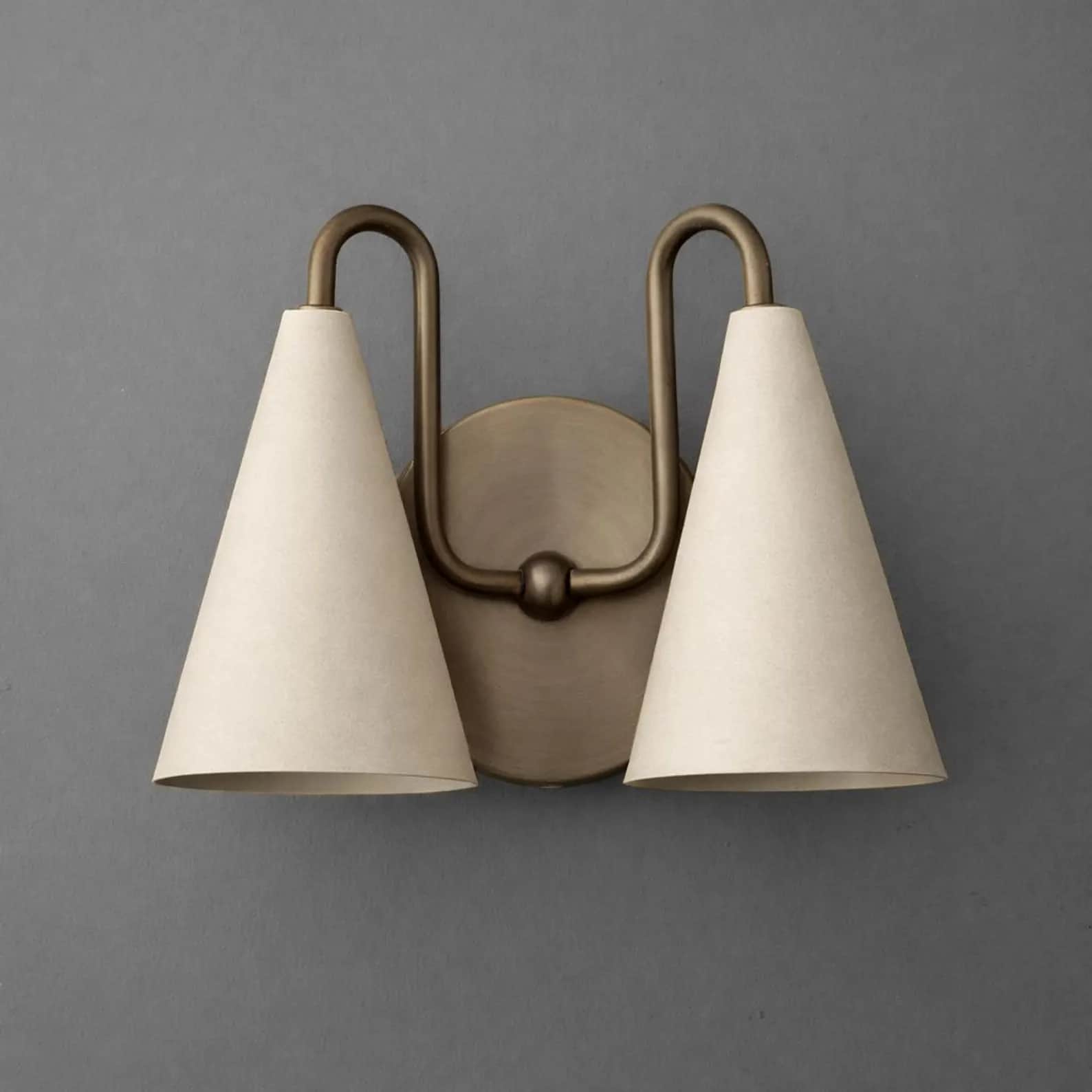 A two-light wall sconce featuring an antique brass finish metal frame and two conical shades. The fi… — 3D model