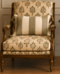 A traditional upholstered armchair with a dark wood frame, featuring botanical patterned fabric and a striped lumbar pillow with tassels. The chair has turned front legs and carved details on the frame. — 3D model
