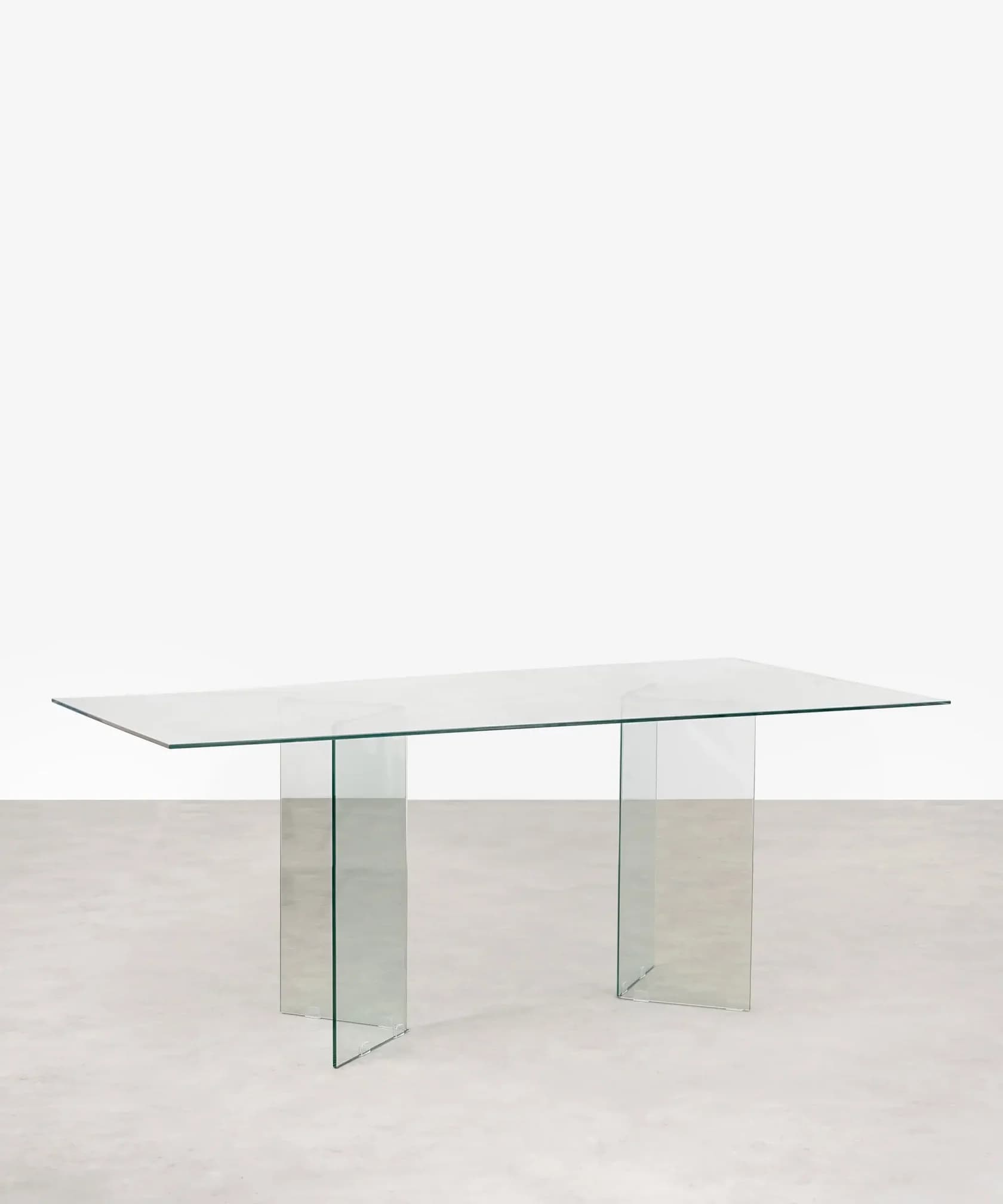 A rectangular table constructed entirely from clear glass, featuring a flat top supported by two distinct angled glass panel bases. — 3D model