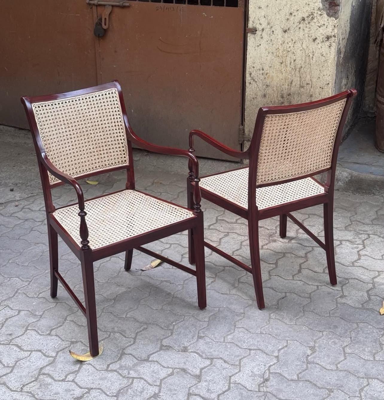 A classic colonial-style armchair featuring a dark-stained wooden frame with a cane woven seat and backrest. The armrests are gently curved, supported by elegantly turned spindles, and the legs are straight. — 3D model