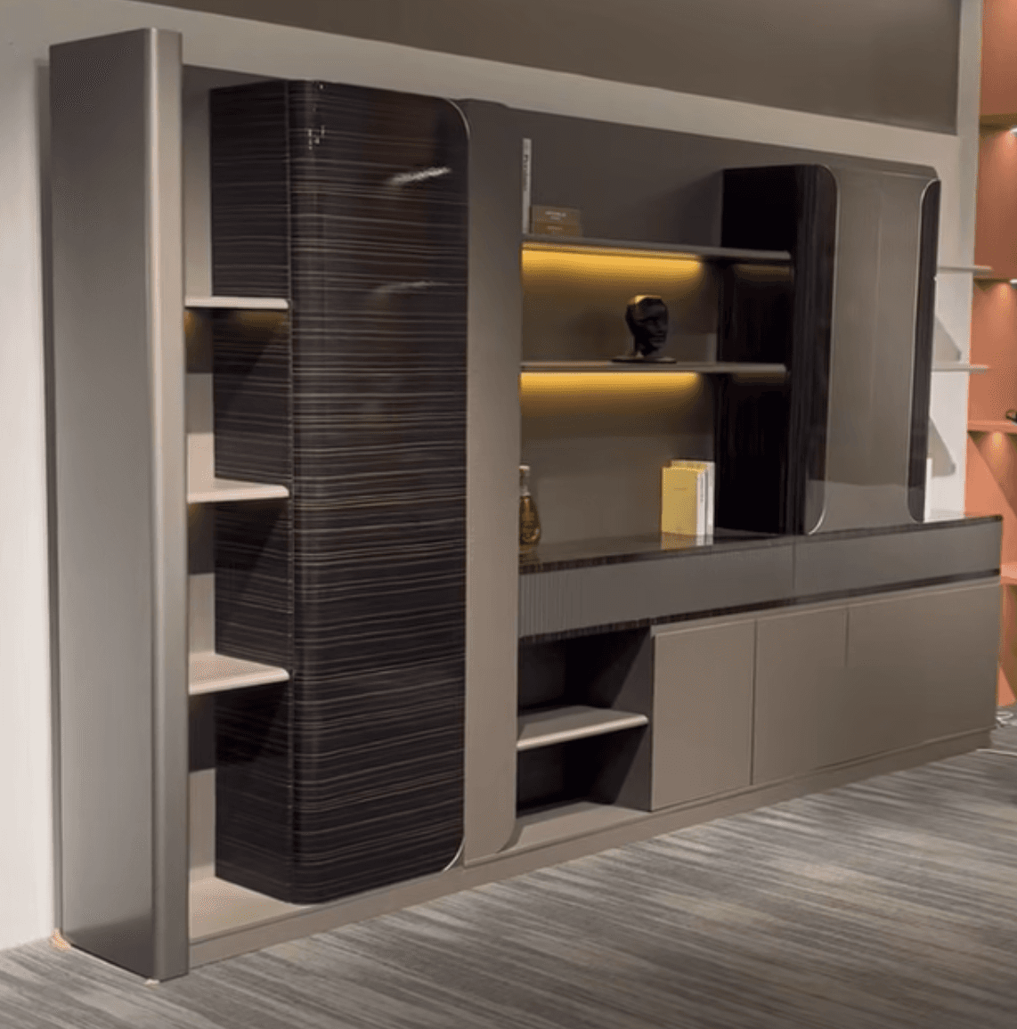 A modern wall-mounted entertainment center featuring a multi-component design with open shelving, enclosed cabinets, and lower drawer storage. The unit combines a taupe/greige finish with dark, horizontally-grained wood accents on some cabinet faces and rounded elements. It includes display niches, illuminated shelves, and fluted textured panels. — 3D model