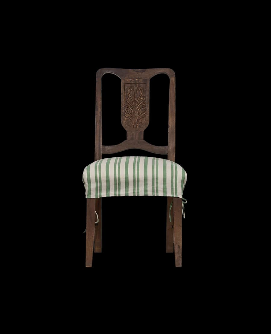 A wooden dining chair with a carved backrest and a striped seat cushion. The chair has a dark wood finish and a backrest with an ornate, symmetrical carving in the center. The seat is covered with a removable cushion featuring alternating green and white stripes. The cushion is secured by ties. — 3D model