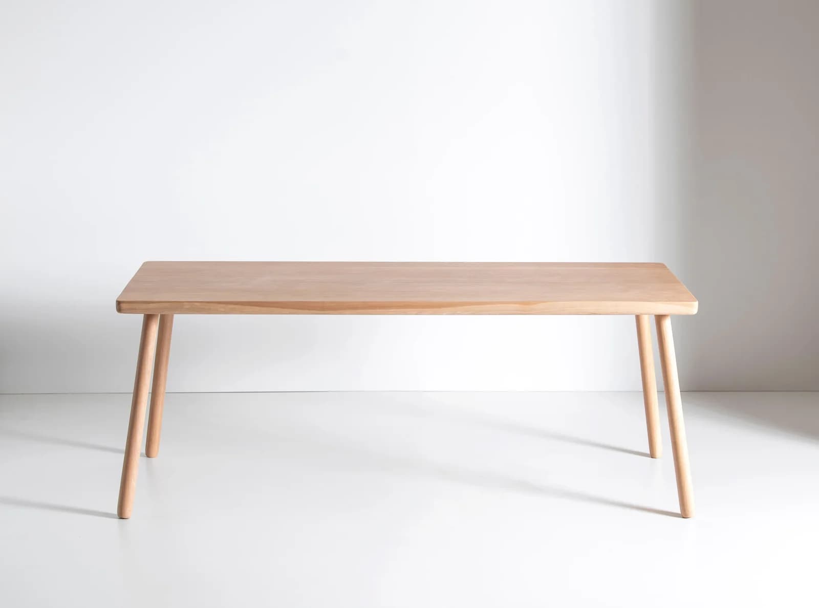 A light-toned wooden rectangular table featuring a smooth top with softly rounded corners and four tapered, cylindrical legs. — 3D model