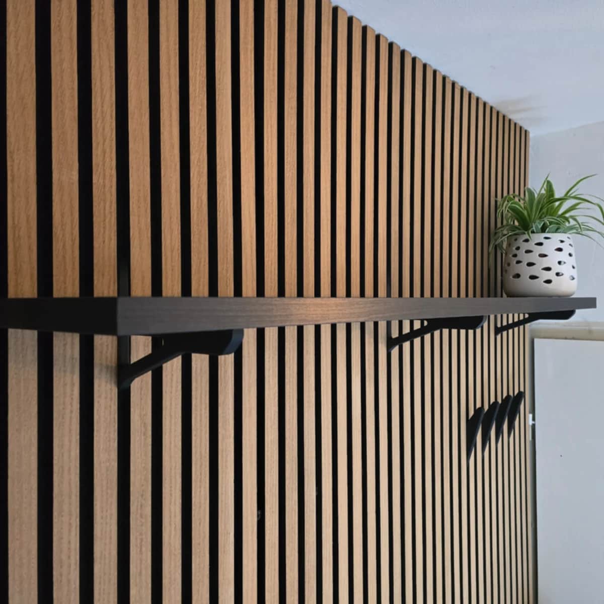 A dark-stained wooden wall shelf mounted on a vertical slatted wood wall panel, supported by two dar… — 3D model