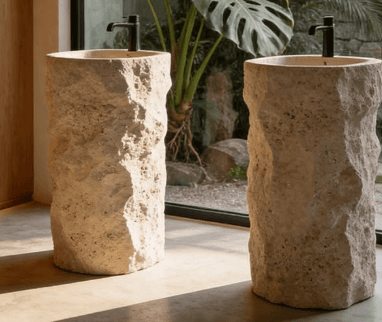 A tall, freestanding pedestal sink made from light-colored, rough-hewn natural stone, featuring an integrated basin and a modern matte black faucet. — 3D model