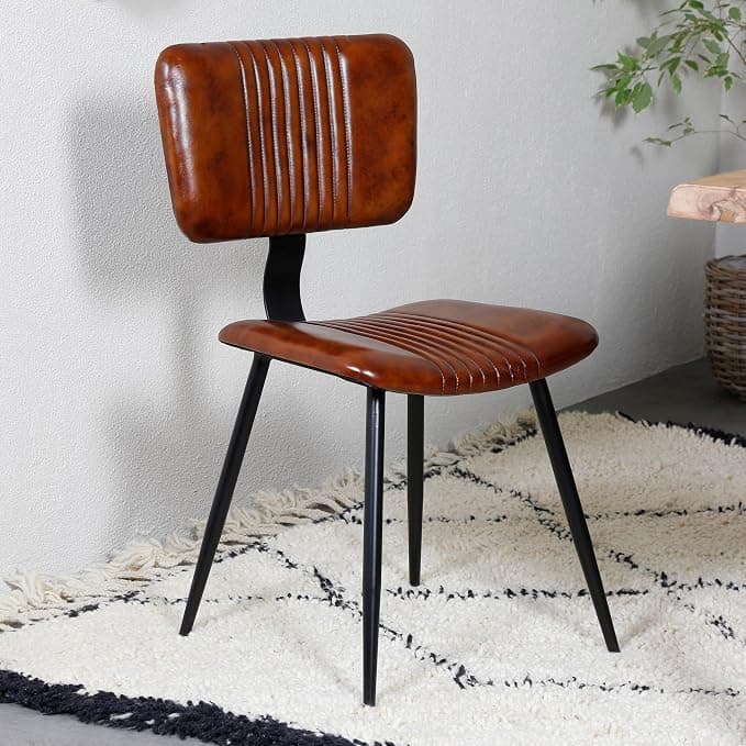 An armless dining chair featuring a contoured seat and backrest upholstered in a rich, distressed brown faux leather. Both the seat and back are adorned with vertical channel-tufting, providing both aesthetic appeal and subtle ergonomic support. The chair is supported by four slender, tapered black metal legs, which splay slightly outwards for stability. The design combines elements of industrial and contemporary styles, suitable for various interior settings. — 3D model