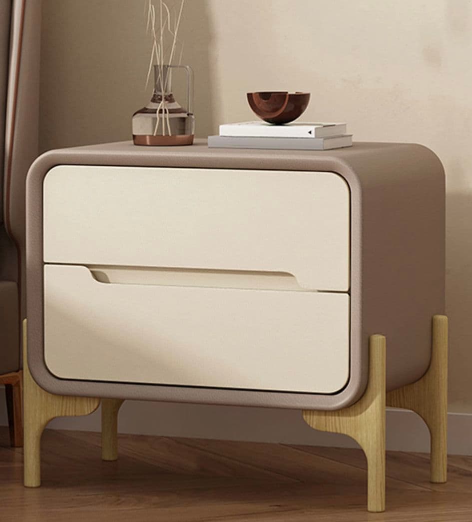 A contemporary two-drawer nightstand featuring a rounded rectangular body in a matte taupe finish. It has two flush-front drawers in a contrasting light beige, each with a subtle integrated cut-out pull. The entire unit is supported by four splayed, round-tapered legs made from light natural wood, providing a modern and elevated aesthetic. — 3D model