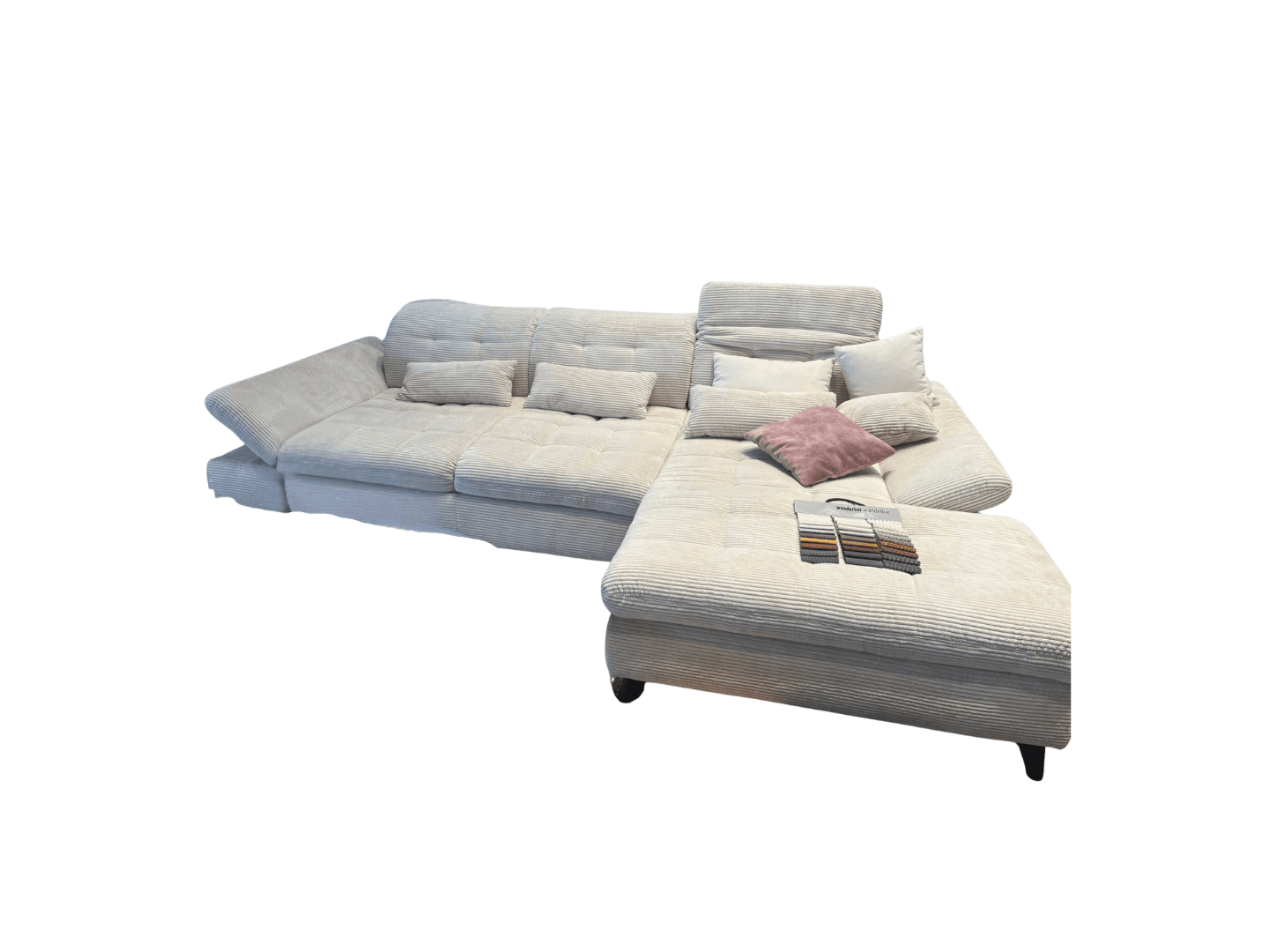 A large, sectional sofa upholstered in a light-colored, corduroy-like fabric. The sofa features deep tufted seat cushions, adjustable headrests, and multiple throw pillows in complementary colors. It has a chaise lounge section and an ottoman-like extension on the right side. A sample swatch book is placed on the surface of the extension. — 3D model