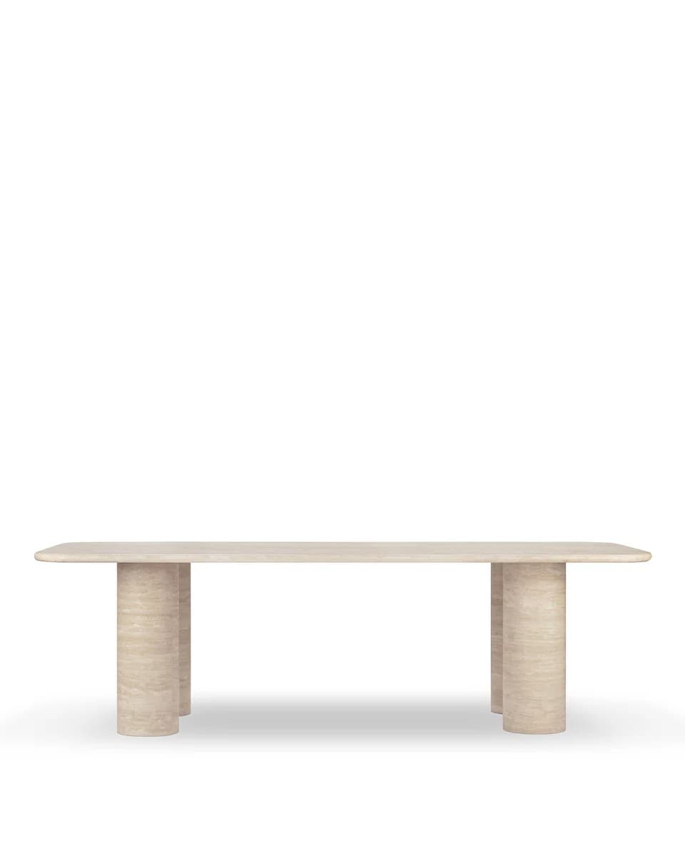 A modern dining table with a rectangular top and rounded corners, supported by four cylindrical legs arranged in pairs. The material appears to be travertine, exhibiting natural variations in color and texture. — 3D model